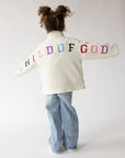 Child wearing a cream fleece pullover with colorful Child of God embroidery across the back and sleeves