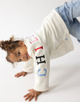 Child leaning sideways in the Child of God cream fleece pullover and blue jeans