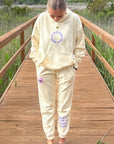 Person wearing a beige hoodie and pants on a wooden boardwalk with nature in the background