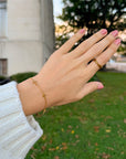 Close-up of gold-tone cross bracelet worn beside evergreen foliage