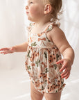 Baby wearing a floral romper and white boots on a plain background