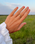 Devotion Ring styled with other rings on a hand against a green field and blue sky