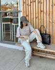 Model seated on a bench wearing the Chateau Grey Disciples Heavyweight Tee with light-colored pants