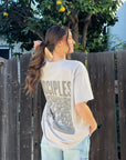 Model showing the Disciples back graphic on a Chateau Grey heavyweight tee beside a wooden fence