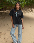 Full-length view of a woman styling the boxy black Christian graphic tee with light blue jeans.