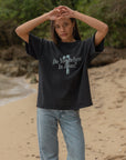 Woman wearing the black Do You Believe in Jesus tee with her arms raised, showing its relaxed boxy shape.