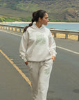 Person wearing a white hoodie and pants with text on a road with a scenic background