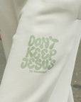 White sweatshirt with green text 'Don't Keep Jesus To Yourself' held by a person.