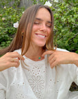 Model wearing the Emerald Agape Cross Pendant Necklace with a white blouse beside garden greenery