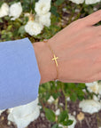 Close-up of the Everlight bracelet’s gold-tone sideways cross worn beside white flowers