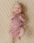Baby in a floral romper lying on a textured beige surface