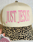 Cap with 'JUST JESUS' text and leopard print visor held by a hand, with a brand tag visible.