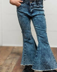 Person wearing a white blouse with ruffled sleeves and blue flared jeans on a wooden floor.