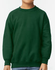 Young boy wearing a forest green Gildan Youth Heavy Blend Crewneck Sweatshirt with a soft fleece interior and classic relaxed fit — perfect for custom prints and cozy everyday wear.