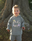 Child standing beside a tree wearing God Made Me kids shorts and a coordinating hoodie