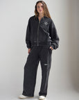 Full-length view of a woman wearing the black God of Miracles zip hoodie with coordinating pants.
