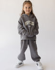 Child modeling Grey Mist God of Miracles sweatpants with a coordinating hoodie and white sneakers