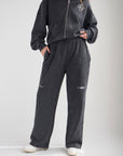 Black God of Miracles wide leg sweatpants with subtle embroidery, styled with a coordinating zip hoodie and light sneakers.