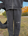 Outdoor close-up of black God of Miracles sweatpants showing the wide legs and embroidered details.