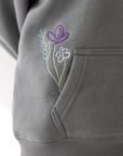 Close-up of colorful floral embroidery beside the front pouch pocket of the Sedona Sage hoodie.