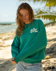 Model wearing the Grace Greenlake sweatshirt with jeans beneath palm trees