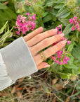 Heart Chain gold-tone ring styled on a hand beside pink flowers and greenery.