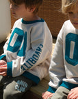 Children wearing Pumice Stone Heaven’s Favorite crewneck sweatshirts with teal number appliqués and sleeve lettering