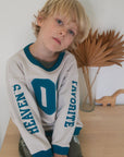 Child wearing the Pumice Stone Heaven’s Favorite crewneck with teal neckline and sleeve accents