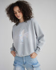 Woman looking down at the pastel cross graphic on her Pearl Blue crewneck sweatshirt