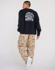 Man wearing black long sleeve heavyweight tee with Windy City Revival back graphic and camouflage pants