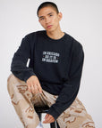 Seated man wearing black In Chicago as It Is in Heaven long sleeve tee with camouflage pants