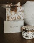 Decorative trinket box with floral design and ribbon, next to a ceramic container on a wooden surface.