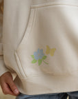 Close-up of pastel floral embroidery beside the kangaroo pocket on the Nimbus Cloud hoodie