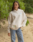 Model wearing the relaxed-fit Jesus Is Alive hoodie in Nimbus Cloud with jeans outdoors