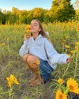 Model crouching among yellow flowers wearing the Jesus Is King Heather Grey Hoodie