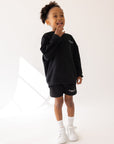 Front view of a child wearing the black Kingdom Club sweatshirt with coordinating shorts and white sneakers.