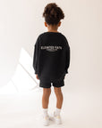 Back view of the oversized Jet Black kids’ sweatshirt styled with black shorts.