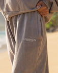 Person wearing a beige hoodie and pants with 'Elevated Faith' logo on a beach.