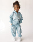 Child modeling the Air Blue Kingdom Kids Hoodie with coordinating pants and white sneakers