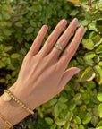 Kingdom gold-tone cross ring worn with other jewelry against green foliage.