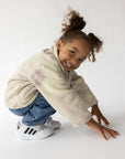 Child crouching in a pearl and mauve marble fleece pullover with jeans and sneakers