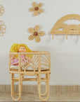 Rattan crib with a doll inside, surrounded by rattan flowers on a white wall.