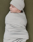 Baby wrapped in a light gray swaddle and cap against a green background
