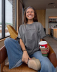 Woman seated indoors wearing grey Not Sorry Jesus Is King tee with blue jeans