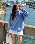 Model wearing the Not of This World blue hoodie with light-colored shorts beside the water