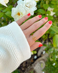 Hand wearing Open Cross Gold-Tone Ring with a cream knit sleeve against white flowers