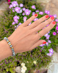 Open Cross Gold-Tone Ring styled with a beaded bracelet beside purple flowers