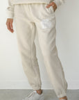 Person wearing a cream-colored tracksuit with white sneakers on a plain background