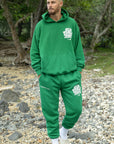 Man wearing a green tracksuit with a logo, standing on a rocky beach.