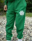 Person wearing green sweatpants with text, standing on a gravel surface.